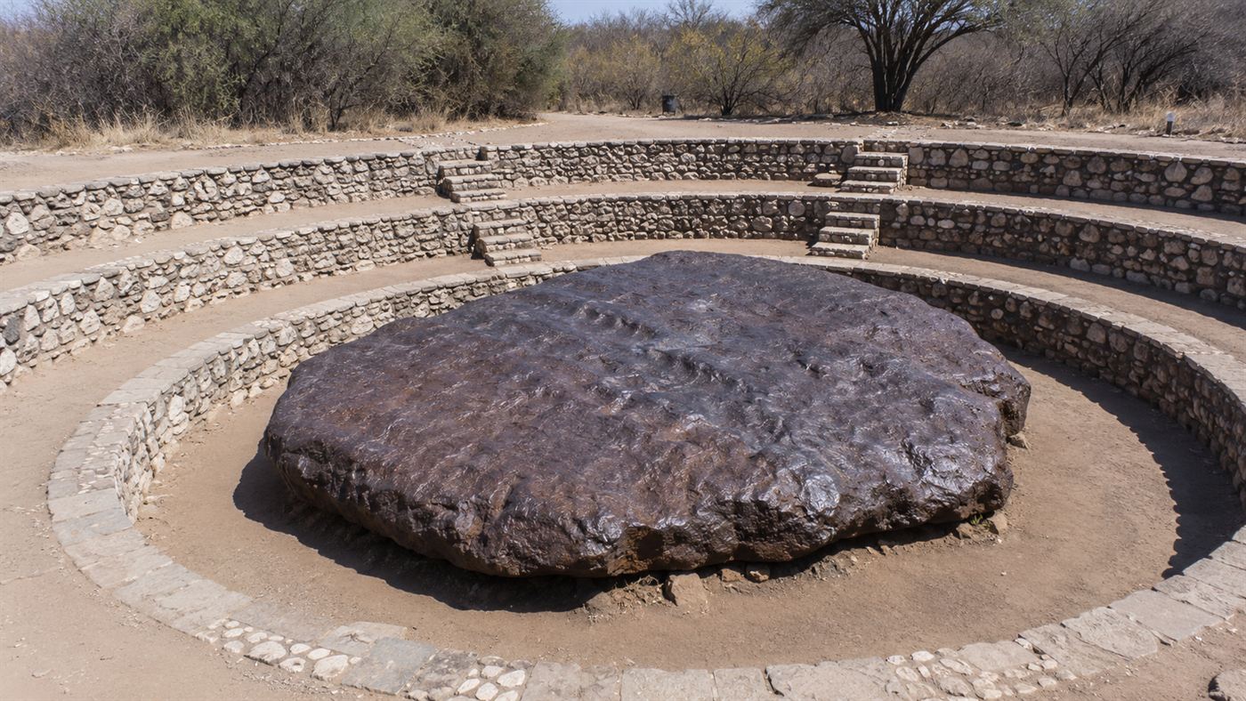 The huge flat dark slab of the Hoba meteorite in a stone amphitheatre in the Namibian bush