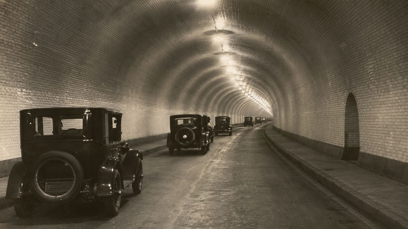 The tiled interior of the Holland Tunnel with early automobiles and rows of ceiling lights