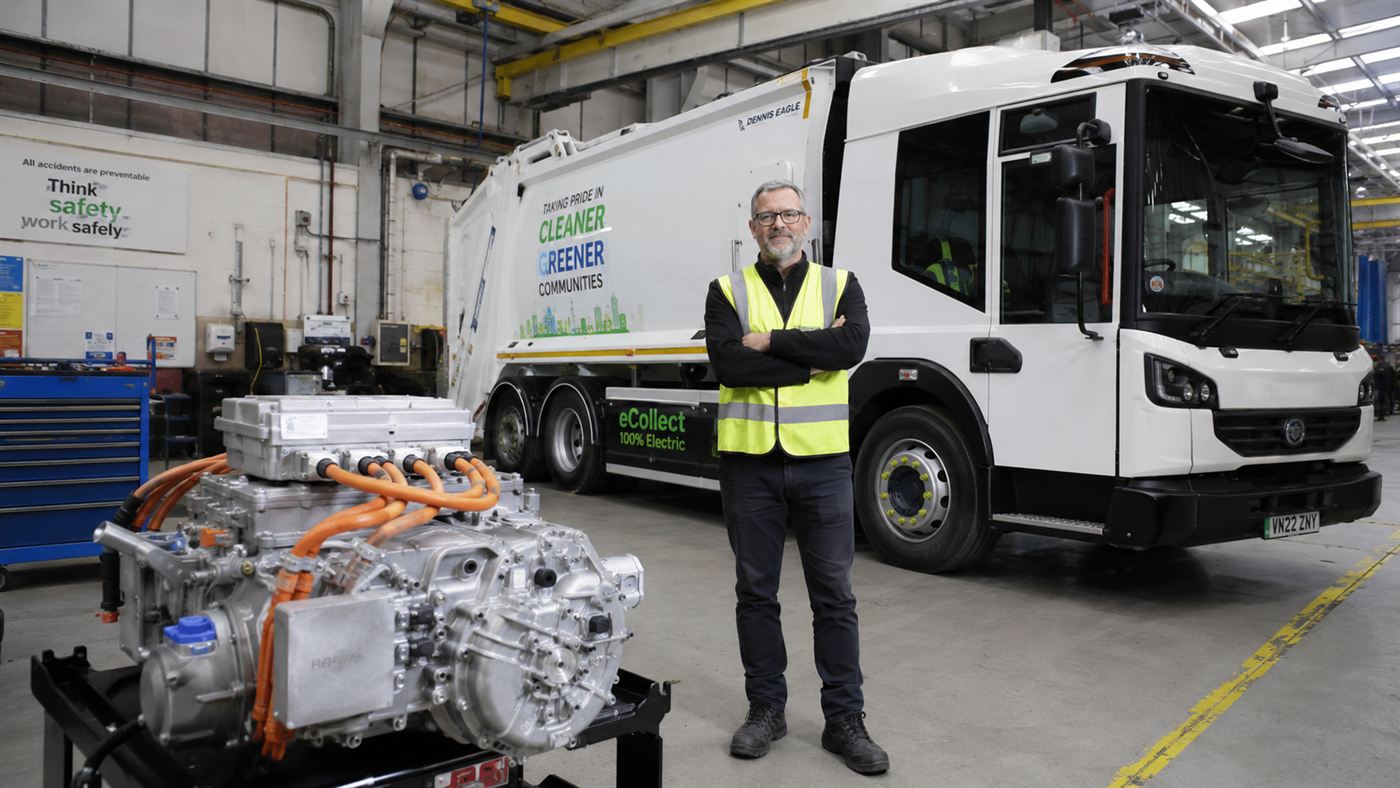 Ian Wright, an engineer in a hi-vis vest, standing beside a garbage truck with an electric powertrain in a workshop