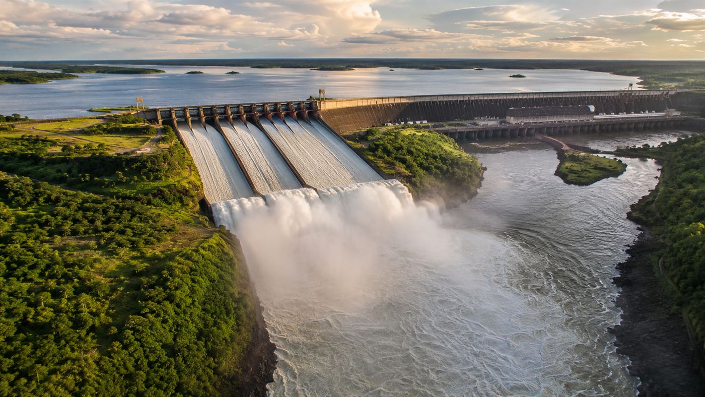 Aerial view of Itaipu dam spanning the Parana River between Brazil and Paraguay, massive concrete structure with spillways releasing white water into the river gorge below