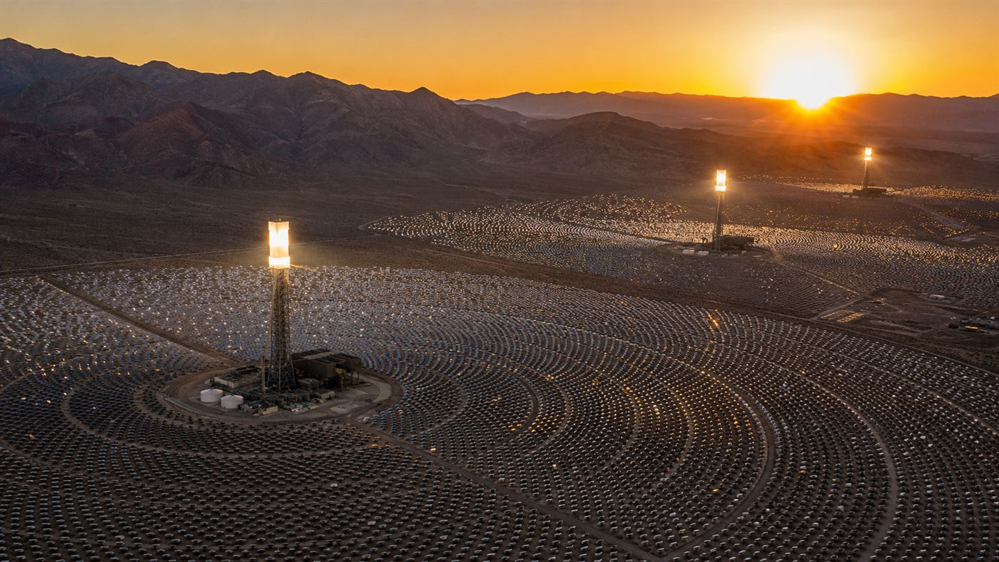 Aerial view of the Ivanpah solar plant in the Mojave Desert at sunset, three glowing towers above the vast heliostat field