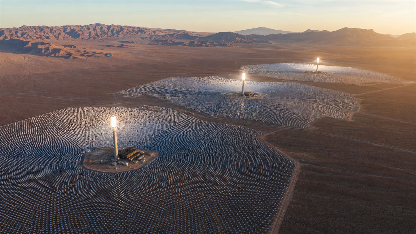 Vast field of silver heliostat mirrors angled toward a central tower rising above the Mojave Desert floor under an intense California sun