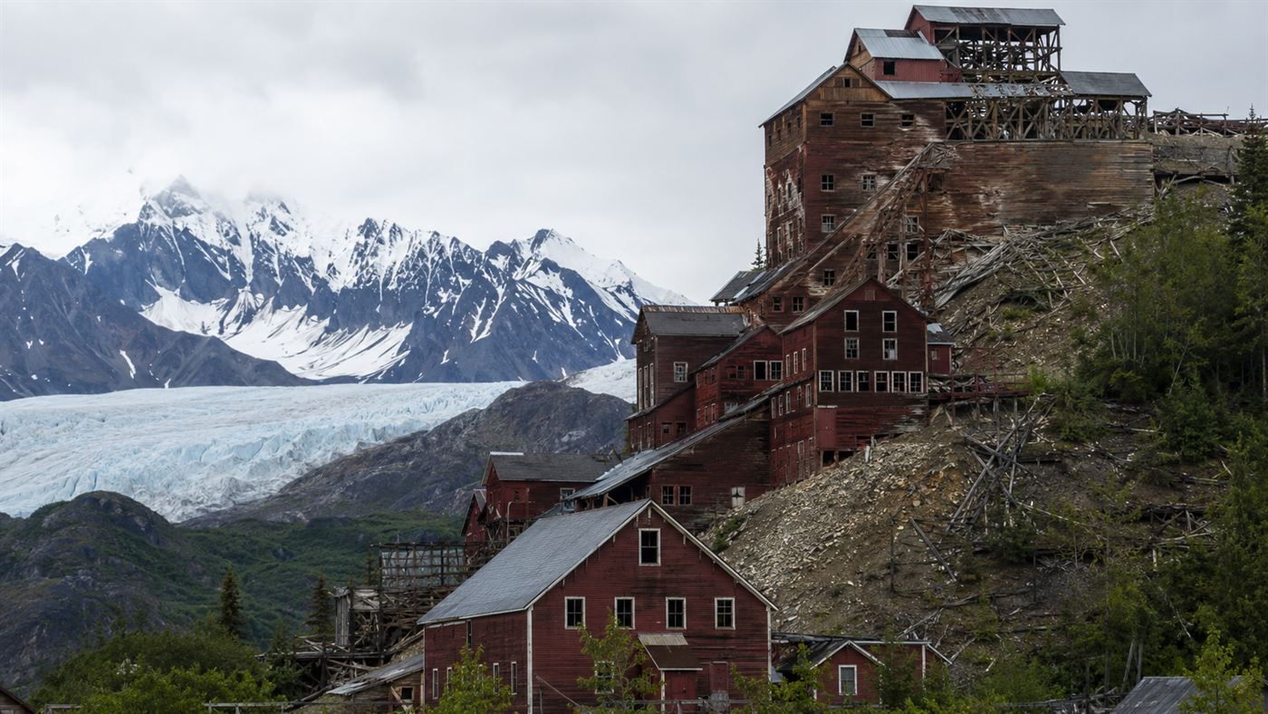 The towering red 14-story concentration mill of Kennecott, Alaska standing against a glacier and snowy peaks