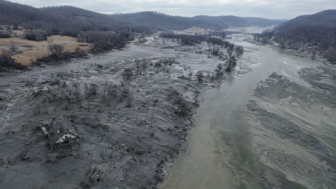A wide aerial view of gray coal ash slurry flooding a Tennessee valley and river after the 2008 Kingston dike failure, burying land and homes