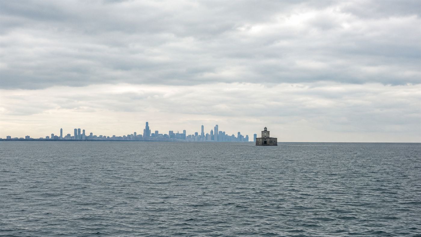 The open grey water of Lake Michigan under an overcast sky with a distant Chicago skyline and an old stone water intake crib far offshore