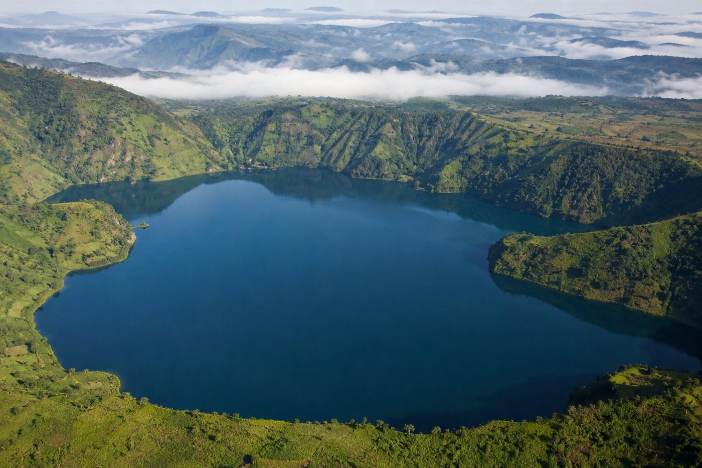 Lake Nyos Cameroon deep blue-green volcanic crater lake surrounded by lush tropical highlands, misty morning, remote landscape
