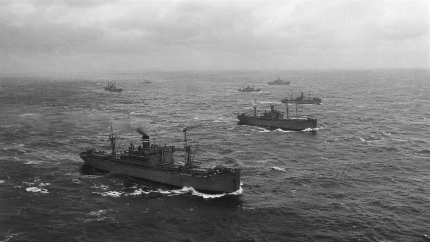 A convoy of grey wartime cargo ships crossing a rough grey Atlantic ocean