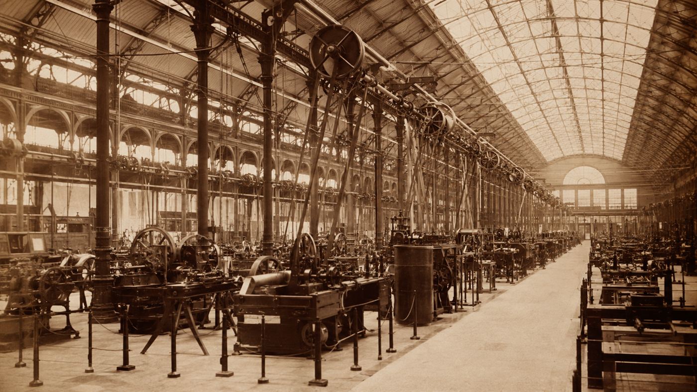 The vast interior of an 1870s machinery hall filled with belt-driven machines and overhead shafting