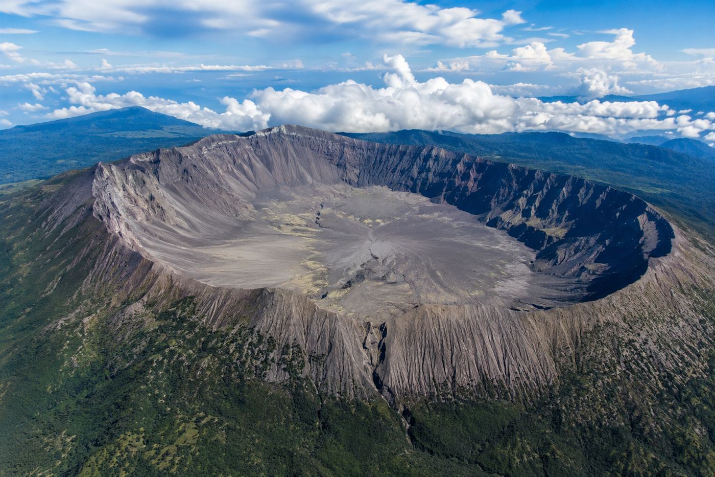 Mount Tambora volcanic caldera aerial view Indonesia, large circular crater with steep gray walls surrounded by tropical rainforest on Sumbawa island, remote volcanic landscape