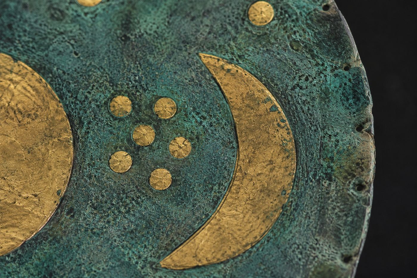 A close-up of the gold symbols on the Nebra sky disc, showing the cluster of seven dots representing the Pleiades beside the crescent