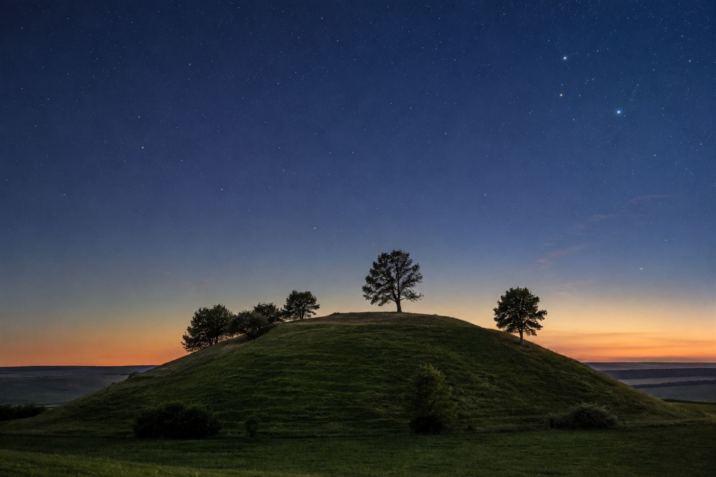 A grassy hilltop in central Germany at dusk with a starry sky above, the kind of place where the Nebra sky disc was buried
