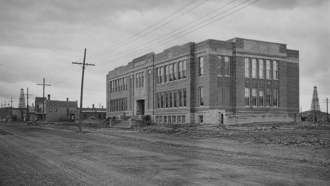 A large 1930s American schoolhouse in an oil-boom town, evoking the site of the New London School explosion