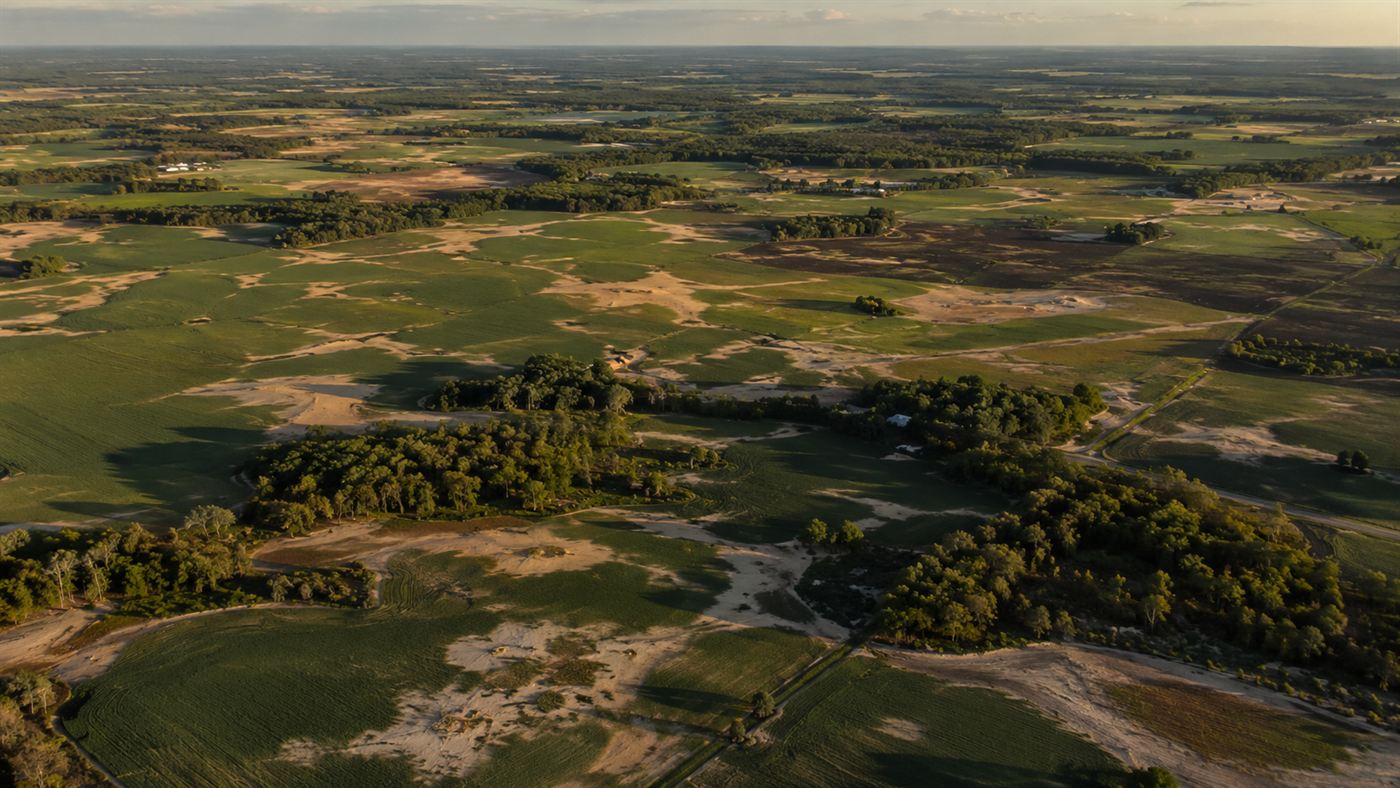 Pale patches of sand spread across a green farm field, the preserved sand blows left by a historic earthquake