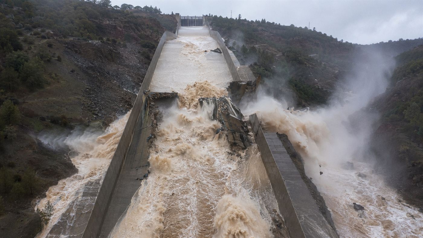 A huge crater torn in the concrete spillway of Oroville Dam with brown floodwater blasting sideways through the broken chute