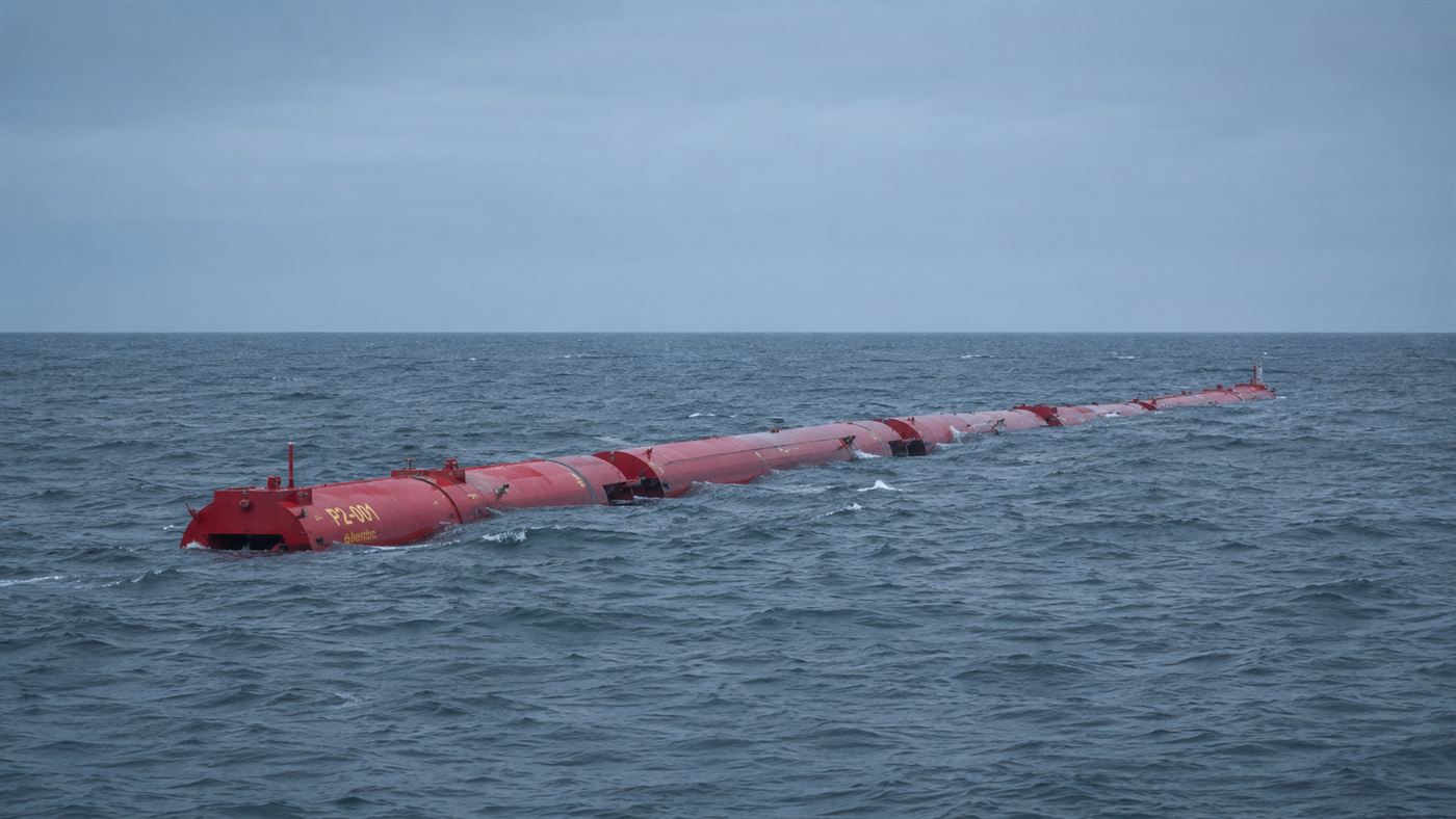 A long red segmented Pelamis sea snake wave energy machine floating on ocean swells offshore