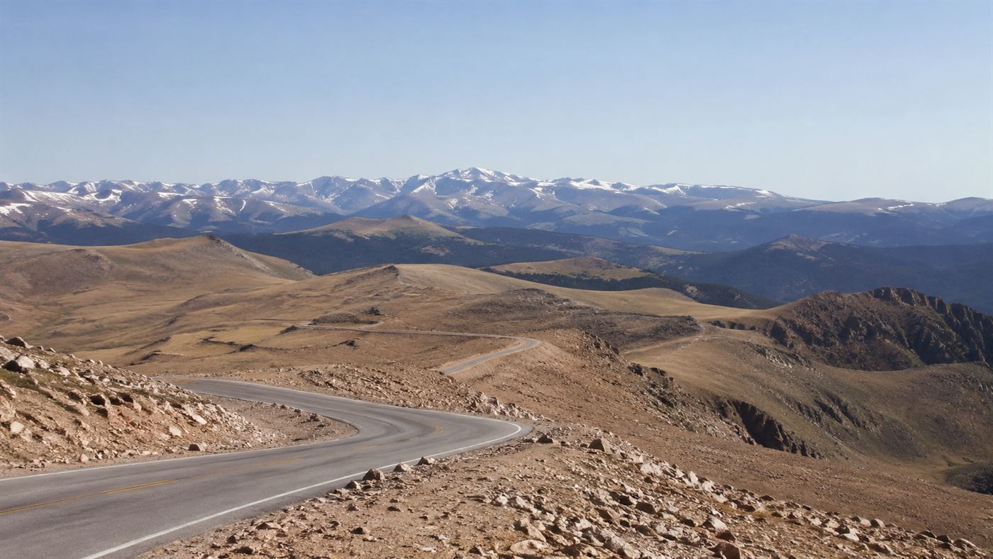 The bare rocky summit road of Pikes Peak high above the treeline with distant mountains under a thin blue sky