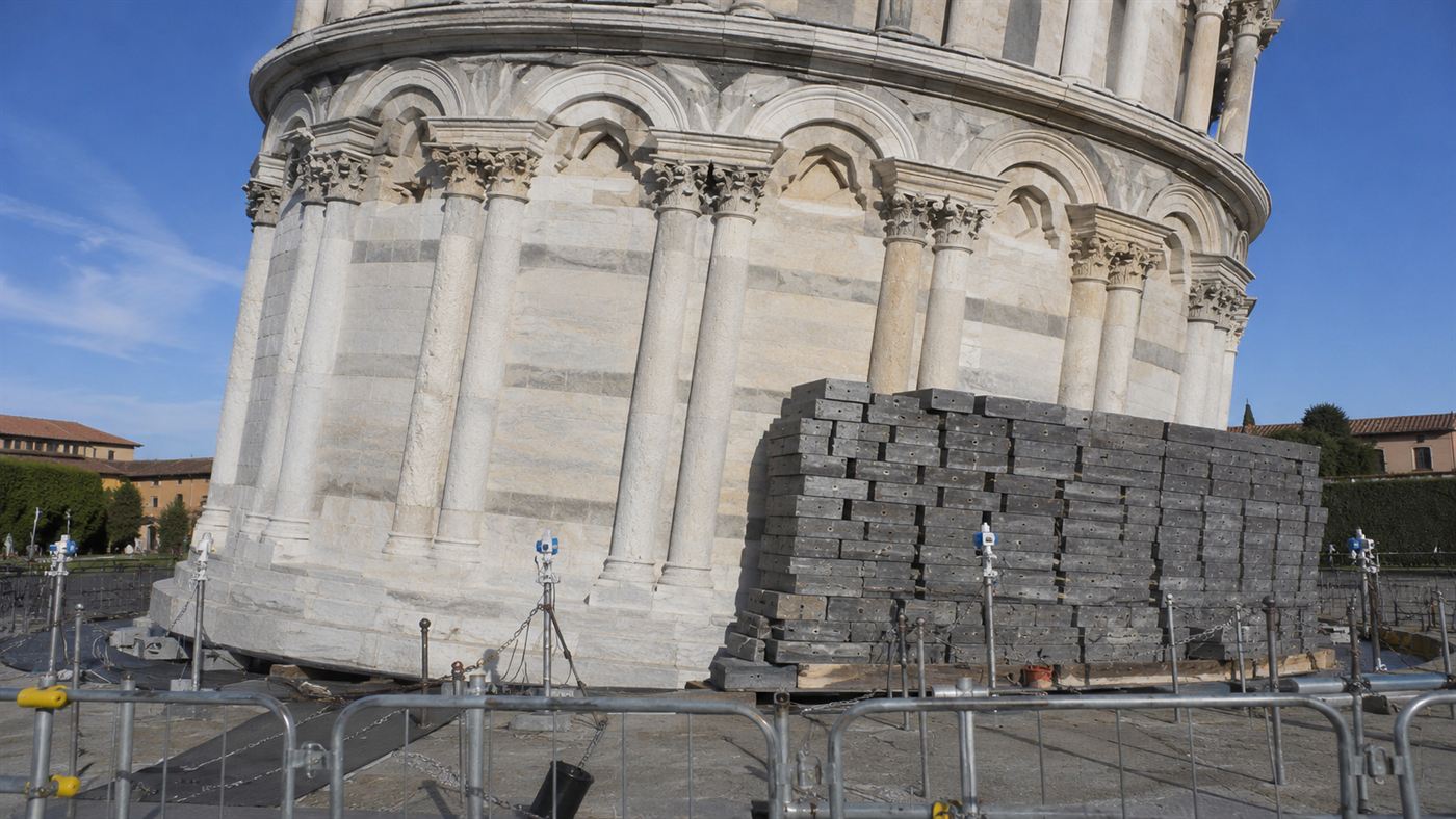 Stacks of grey lead counterweight ingots piled against the base of the Leaning Tower of Pisa as a temporary brake