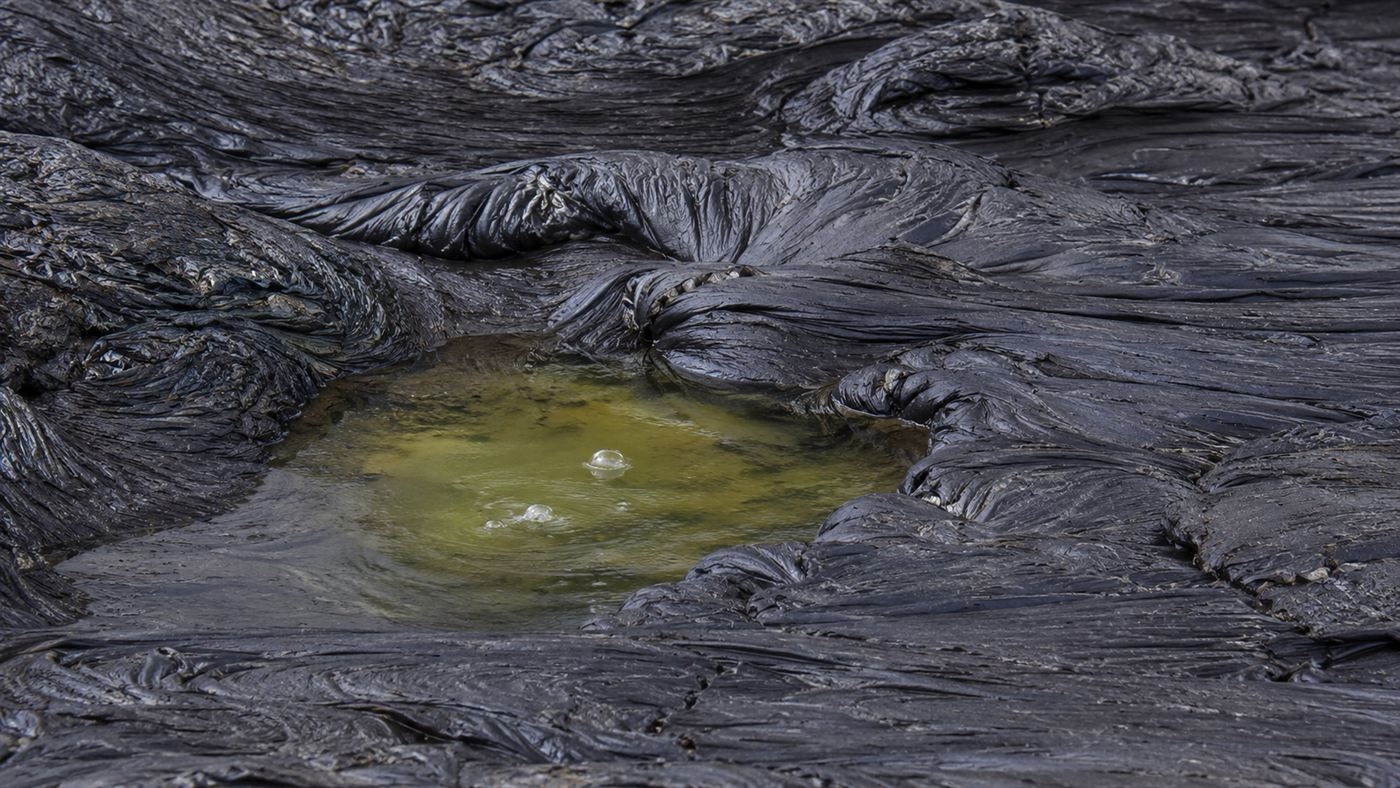 Close view of the wrinkled grey-black semisolid surface of Pitch Lake with coloured water pools