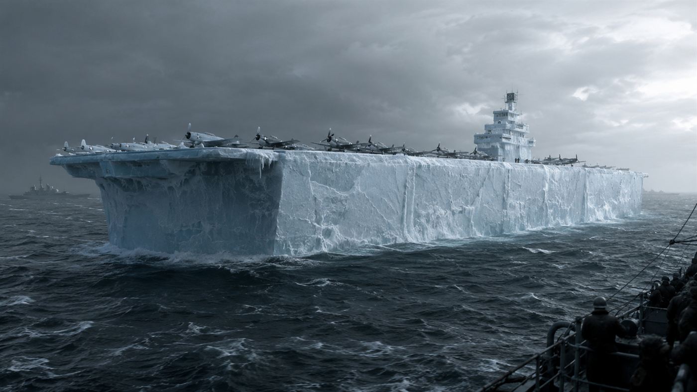 A huge slab-sided aircraft carrier made of ice floating in a grey wartime sea with planes on its deck