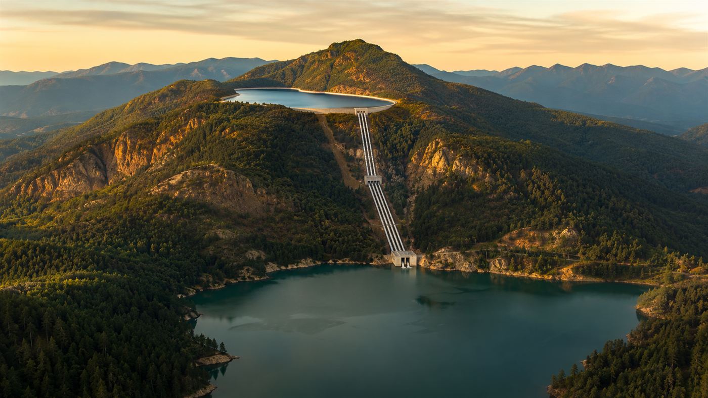 A forested mountain with an upper reservoir near the summit and a larger lower reservoir in the valley, the two lakes of a pumped storage water battery