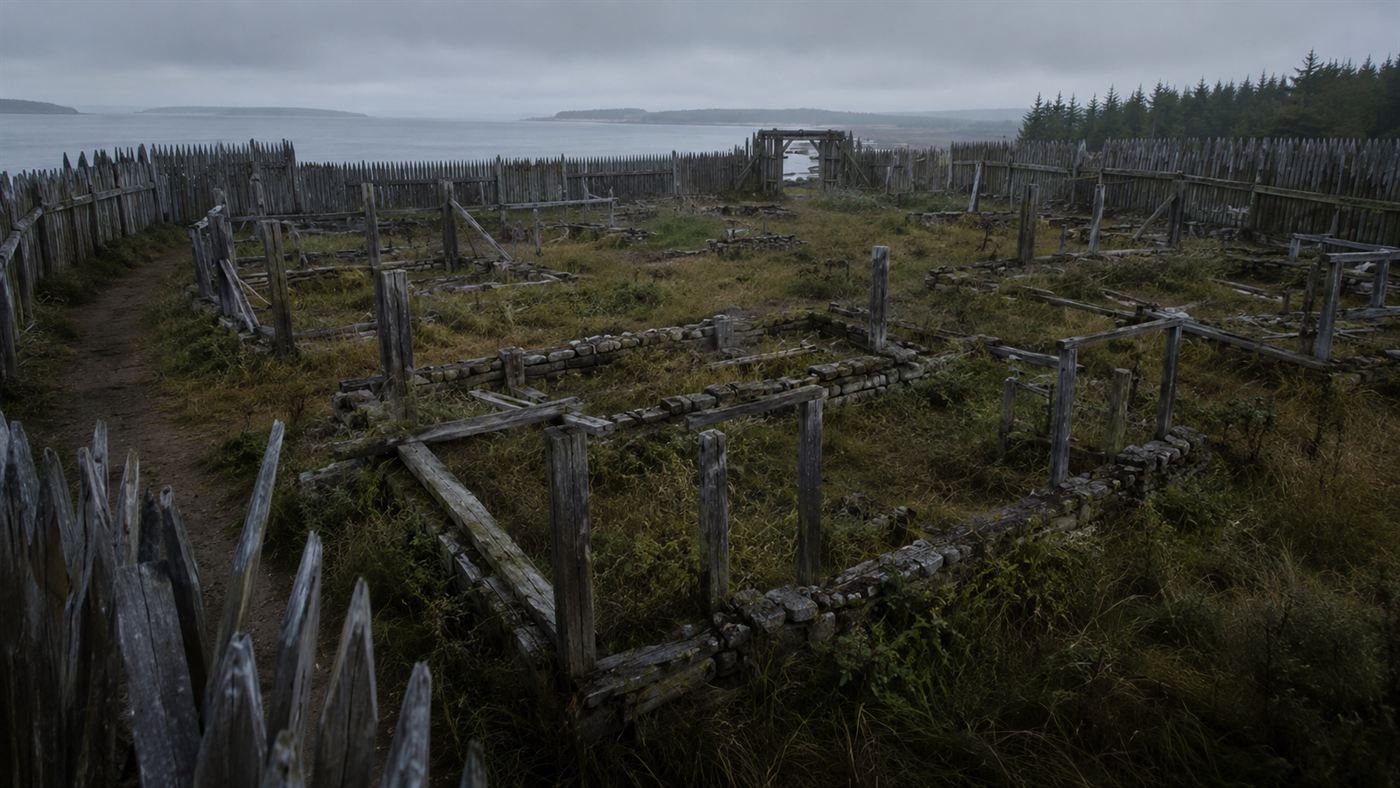 An empty, overgrown palisade enclosure with dismantled house frames at a deserted 1590s coastal settlement