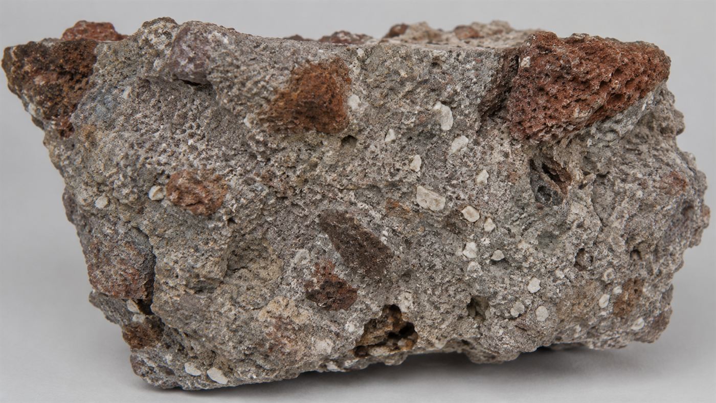 Close-up of ancient Roman concrete showing white lime clasts and reddish volcanic rock embedded in grey mortar