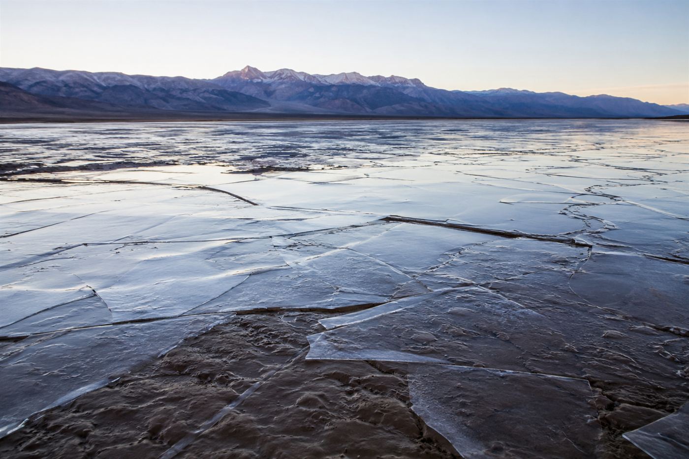A thin sheet of ice over shallow water on a desert dry lake bed at dawn in Death Valley