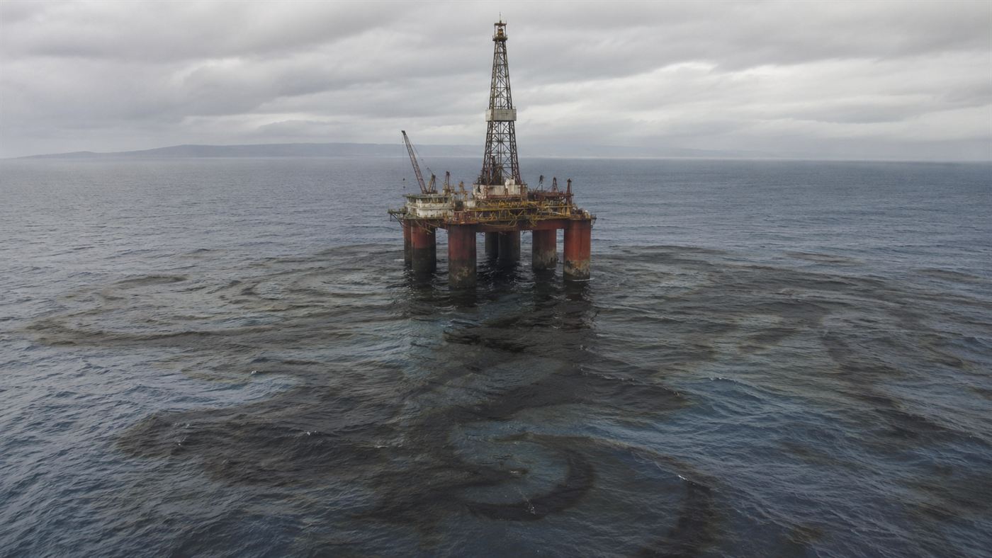 An offshore oil drilling platform in the ocean with a dark oil slick spreading across the water around it in 1969