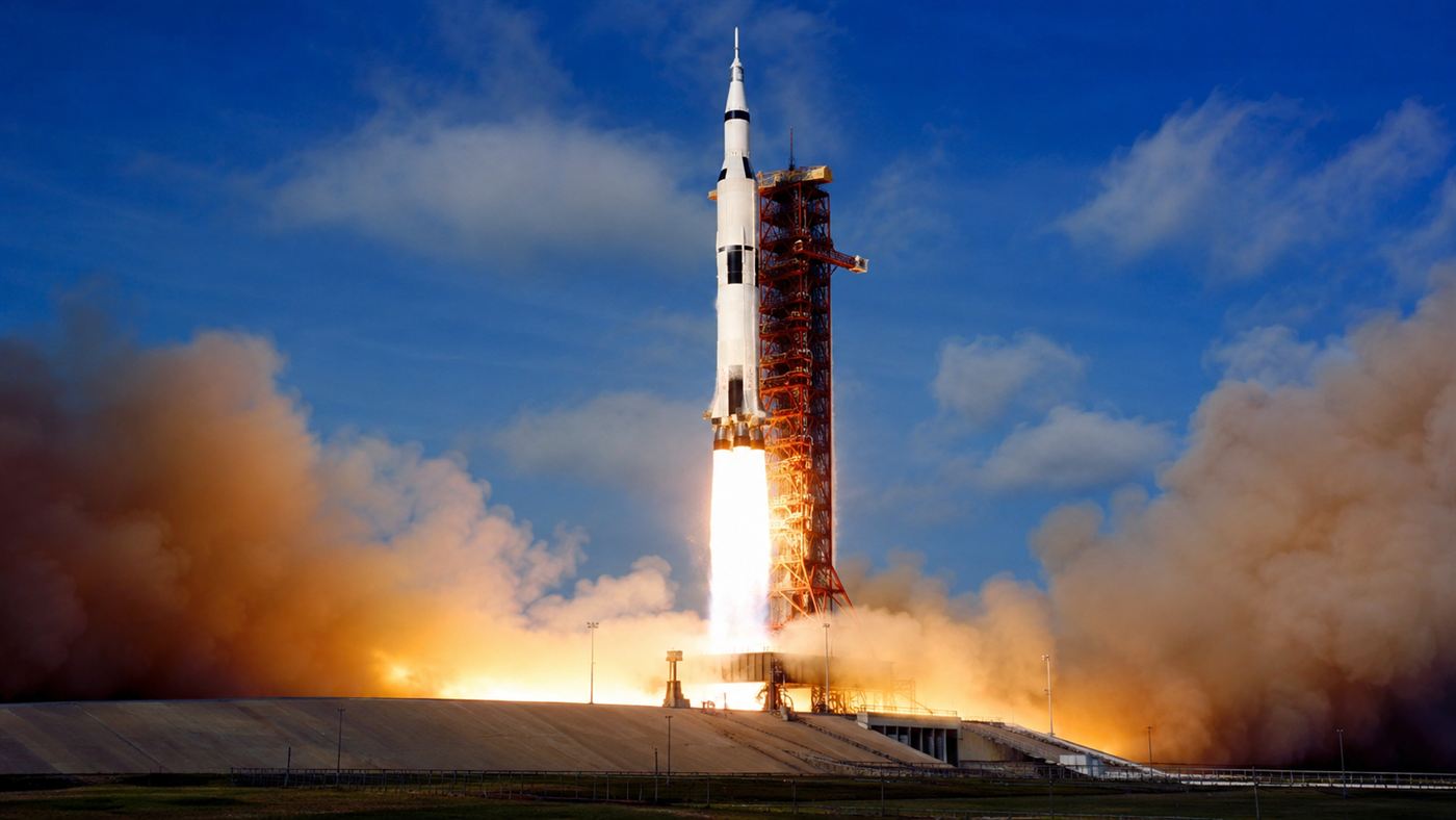 A giant Apollo-era Saturn V rocket lifting off on a massive column of fire and smoke