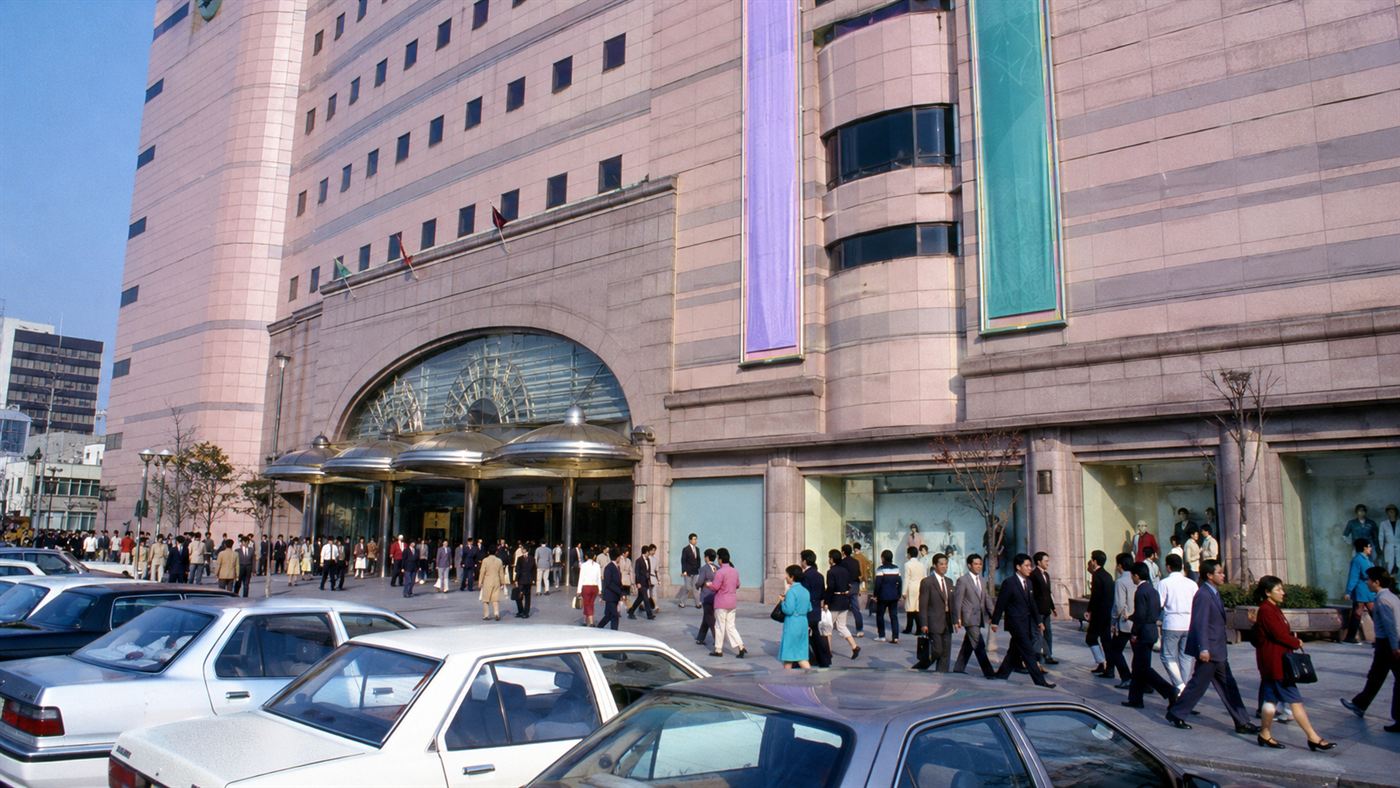 The busy facade of a large multi-story 1990s department store in Seoul with shoppers outside