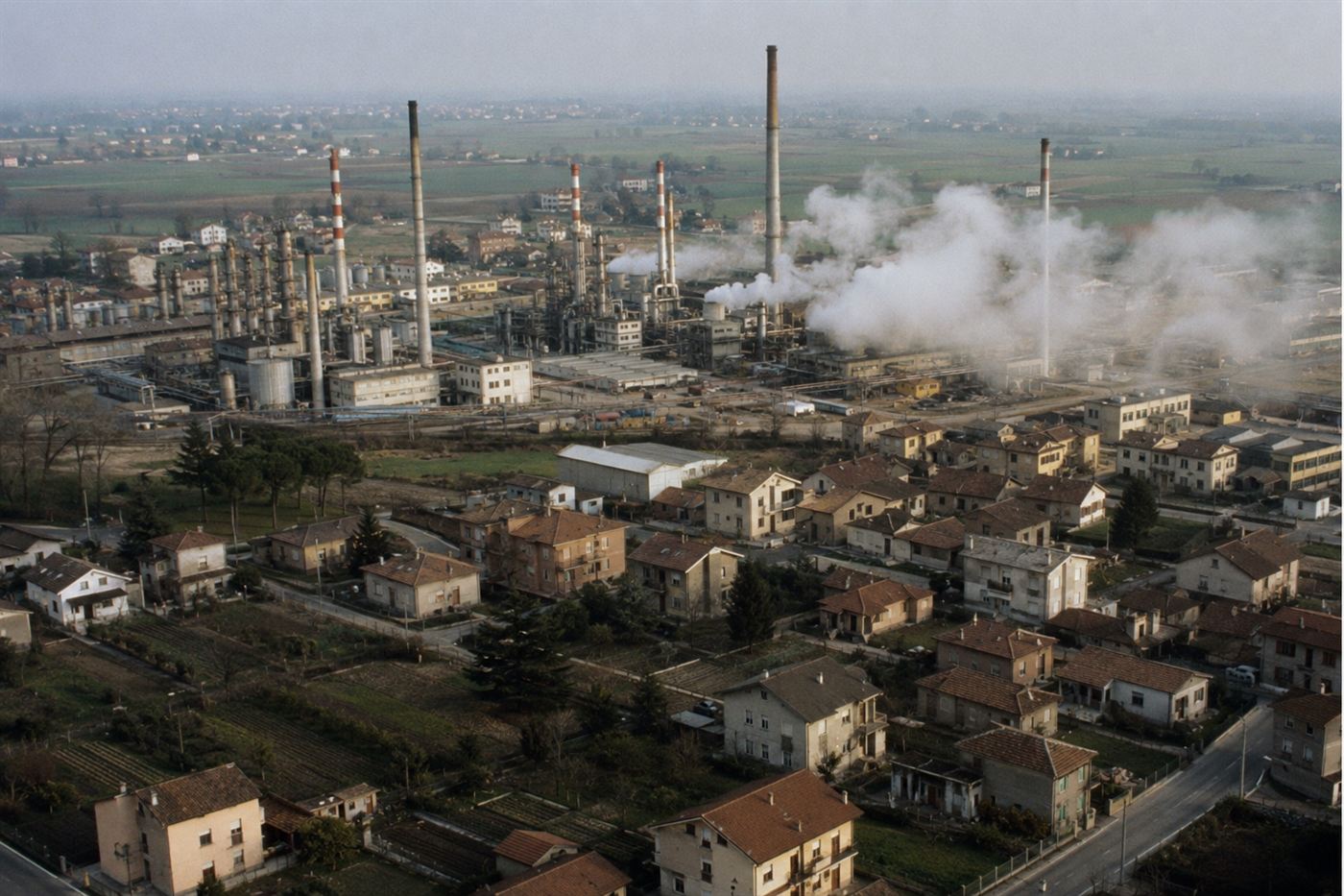 Seveso disaster 1976 ICMESA chemical factory northern Italy, industrial chemical plant with tall chimneys and vapor plume over Italian residential town, Lombardy countryside