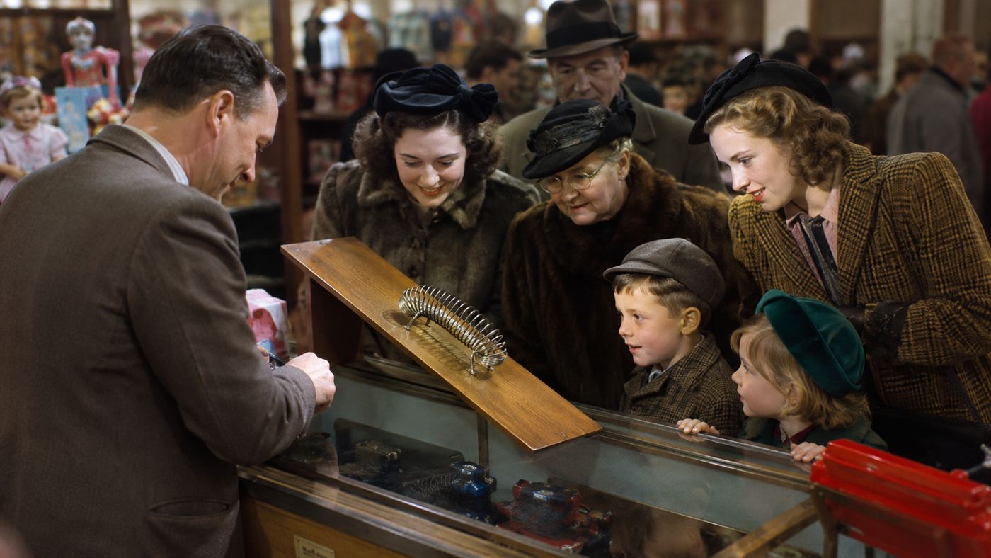 A 1940s department store display where a metal coil toy walks down a small wooden ramp before curious shoppers