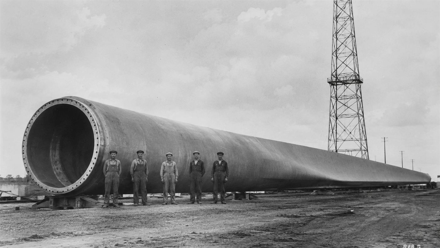 Workers standing beside one enormous steel blade of the Smith-Putnam wind turbine in the 1940s