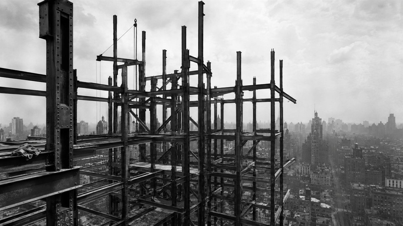 The exposed steel girder frame of an early skyscraper under construction against a city sky