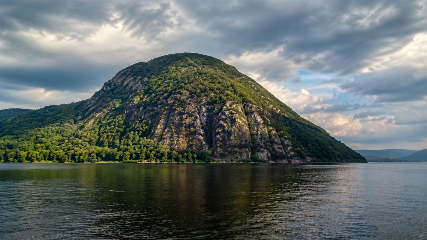 Storm King Mountain rising steeply above the Hudson River under a dramatic sky