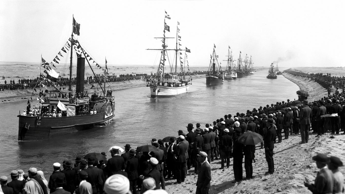 A fleet of decorated ships passing through the Suez Canal at its grand opening ceremony in 1869