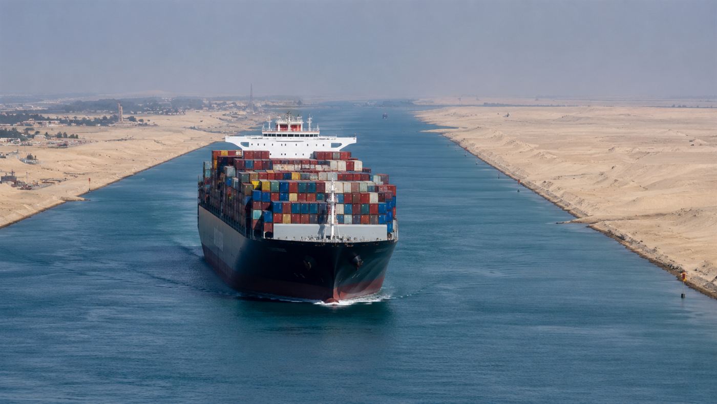 A large container ship moving through the Suez Canal flanked by open desert