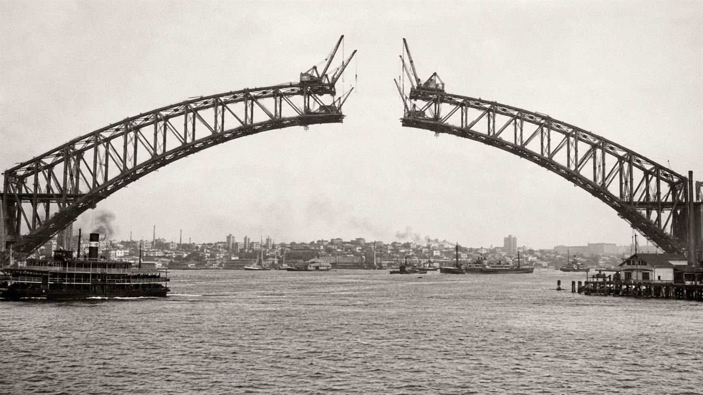 The two half-arches of the Sydney Harbour Bridge under construction reaching toward each other across the harbour