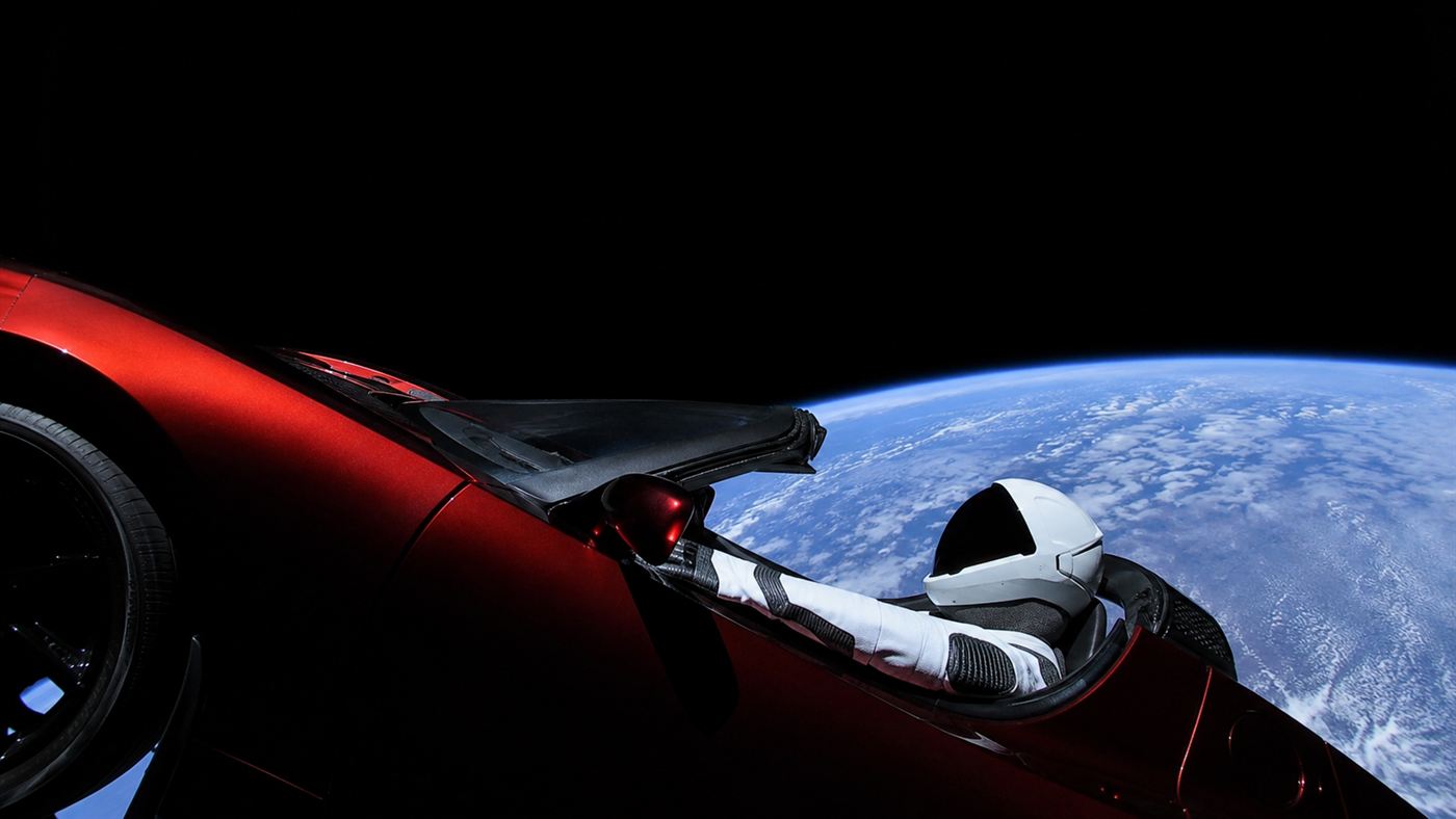 The cherry-red Tesla Roadster in space with a spacesuited Starman dummy at the wheel, Earth behind