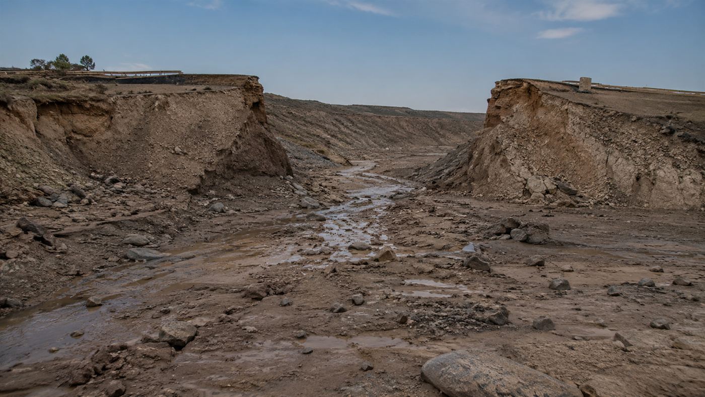 The eroded remains of the Teton Dam after the 1976 failure, a huge gap and scarred earthen abutments in the dry canyon
