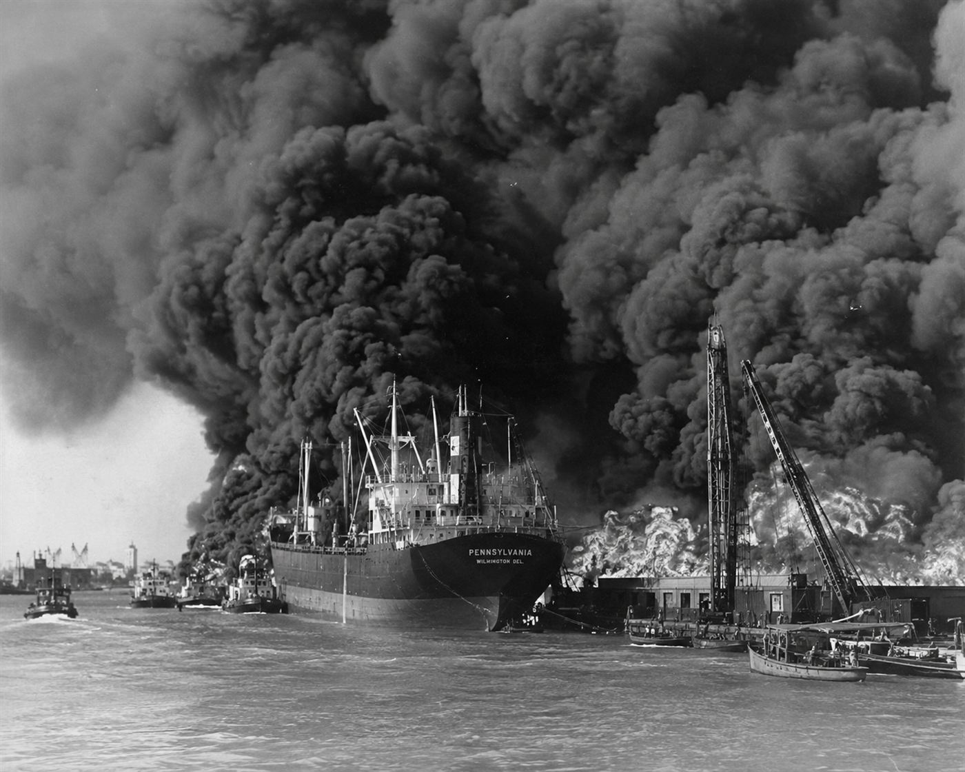 A large cargo ship sending enormous black smoke columns into the sky over an American harbor, massive industrial fire on the dockside in 1947, dramatic morning light over Texas City port