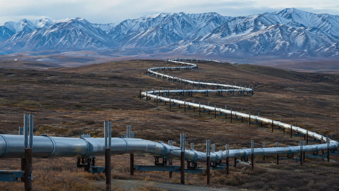 The elevated silver Trans-Alaska Pipeline zigzagging across Arctic tundra on metal support legs with mountains behind