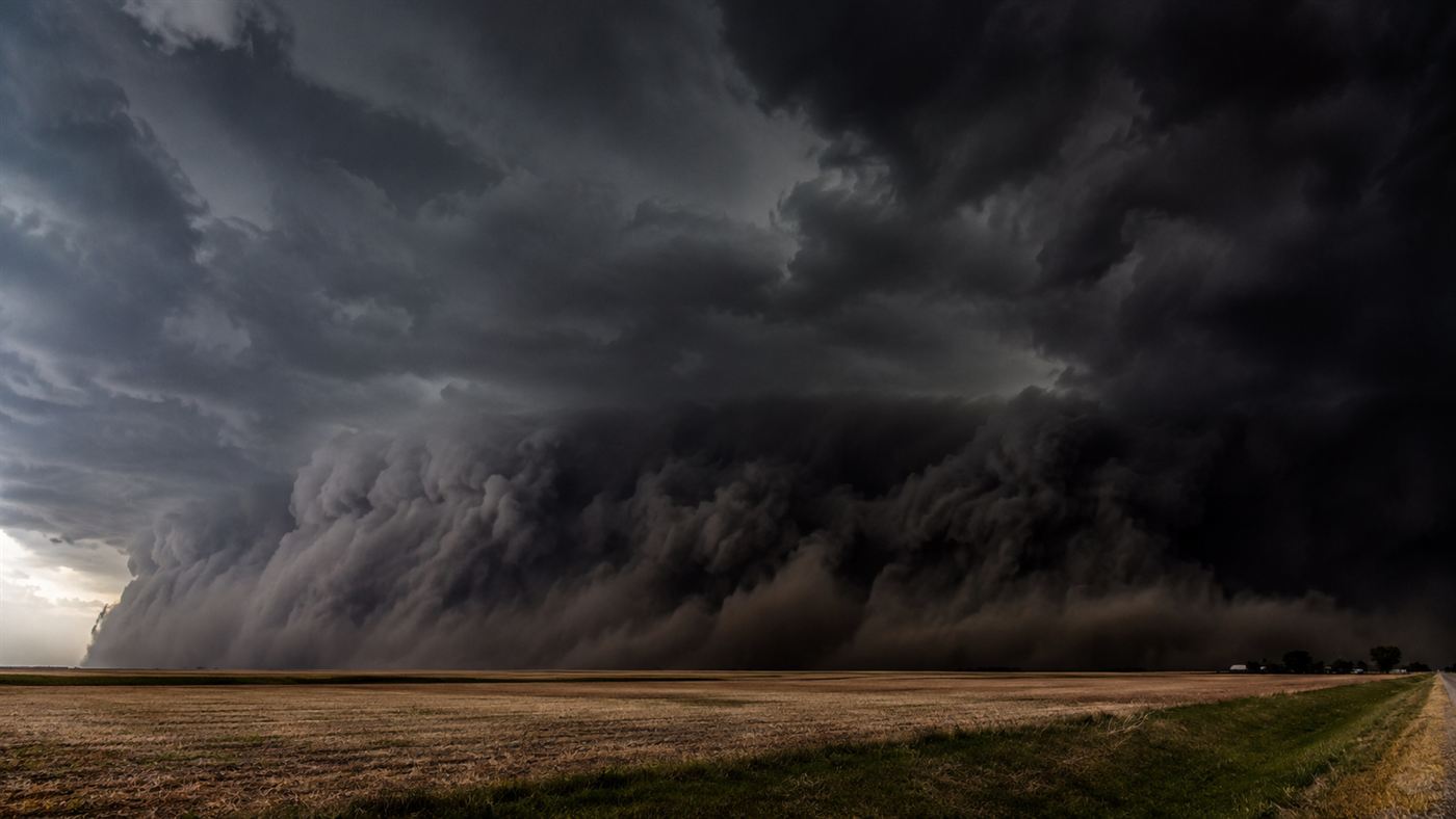 A vast dark rolling wall of cloud and dust advancing across flat Midwestern farmland, not shaped like a classic funnel