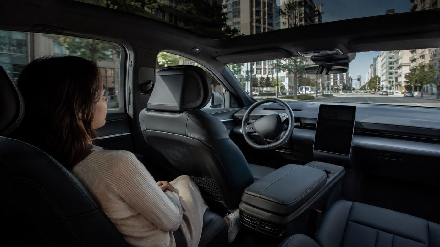 A passenger relaxing in the back of a driverless car while the empty driver's seat and steering wheel turn on their own