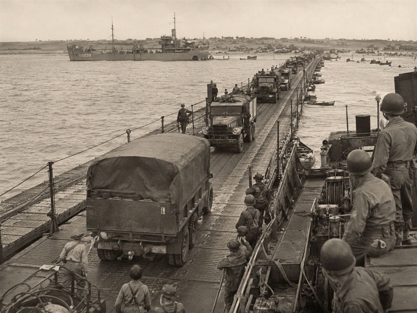 Trucks driving along a floating Whale roadway from a ship to the Normandy beach, part of the Mulberry harbours
