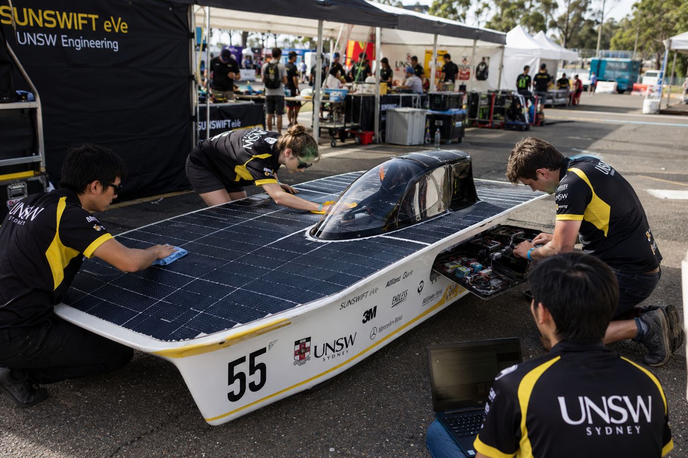 A university student team in matching shirts working on their solar race car, checking the panels and electronics