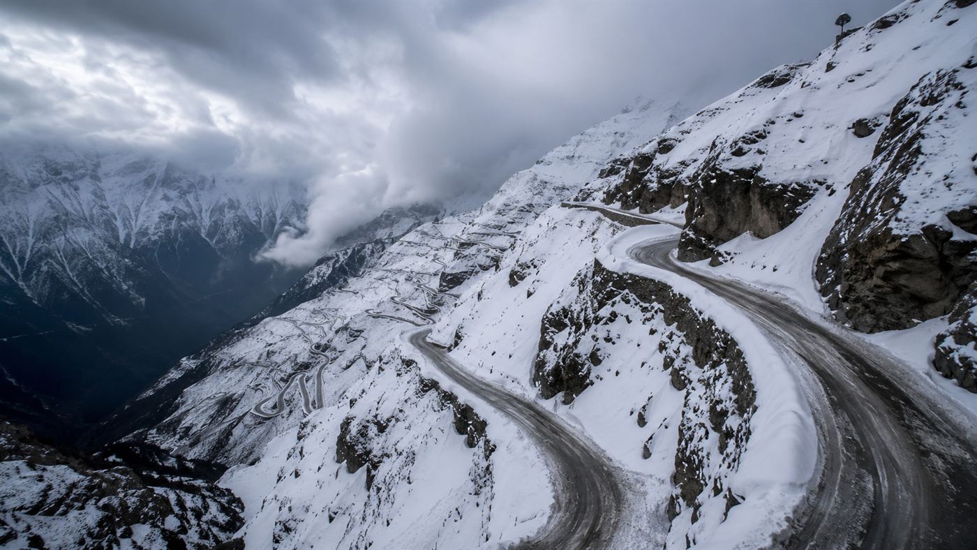 A treacherous snowbound Himalayan mountain pass road with hairpin switchbacks above a deep valley
