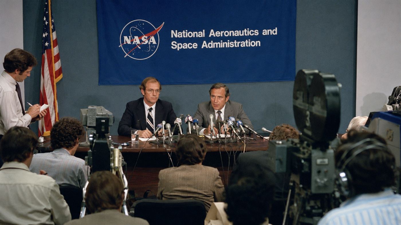 A 1980s science press conference with two scientists at a table of microphones facing reporters