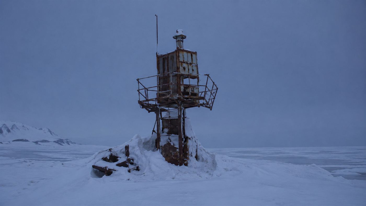 A derelict navigation beacon tower half-buried in deep snow on a remote frozen shore