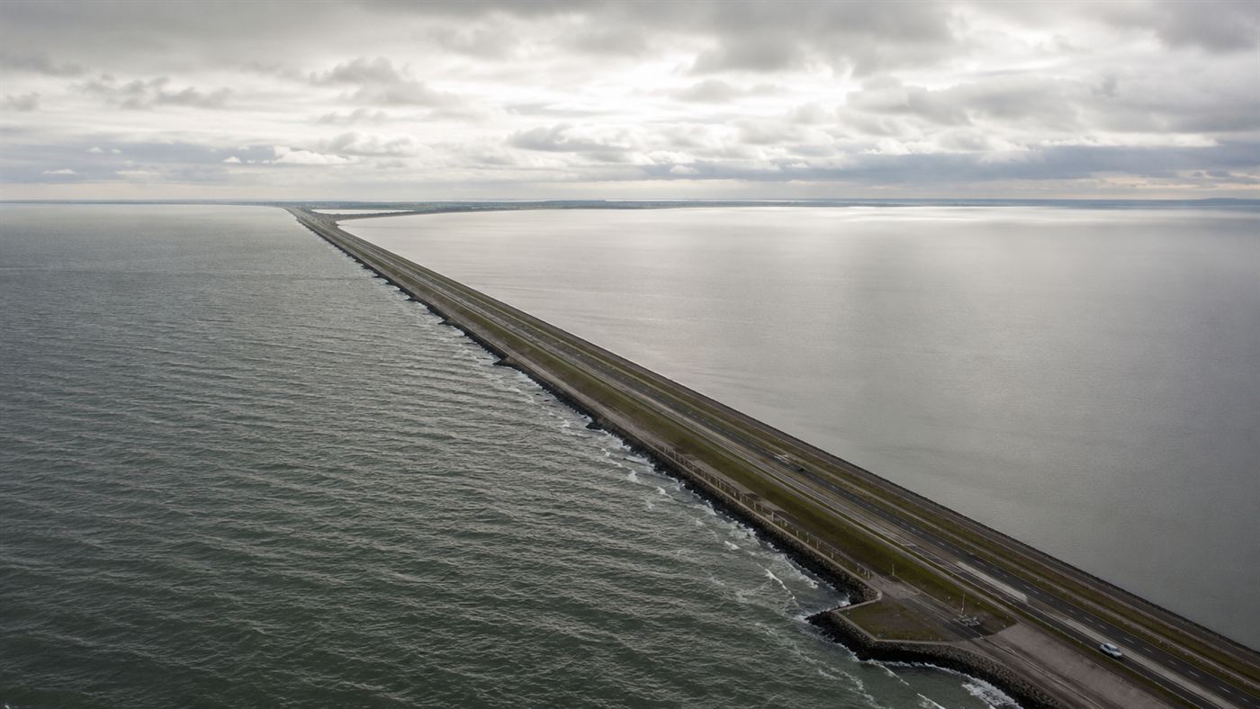 Aerial view of the Afsluitdijk, the long straight dam that sealed off the Zuiderzee, with open sea on one side and a calm lake on the other